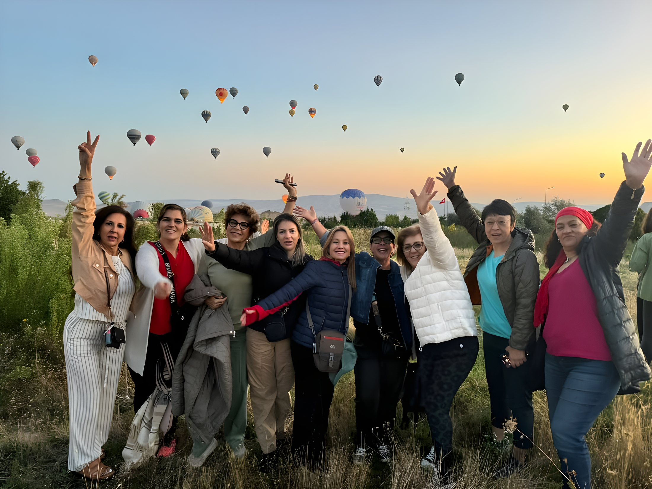 Grupo de viajeras con los brazos en alto al amanecer en Capadocia, con globos aerostáticos en el cielo