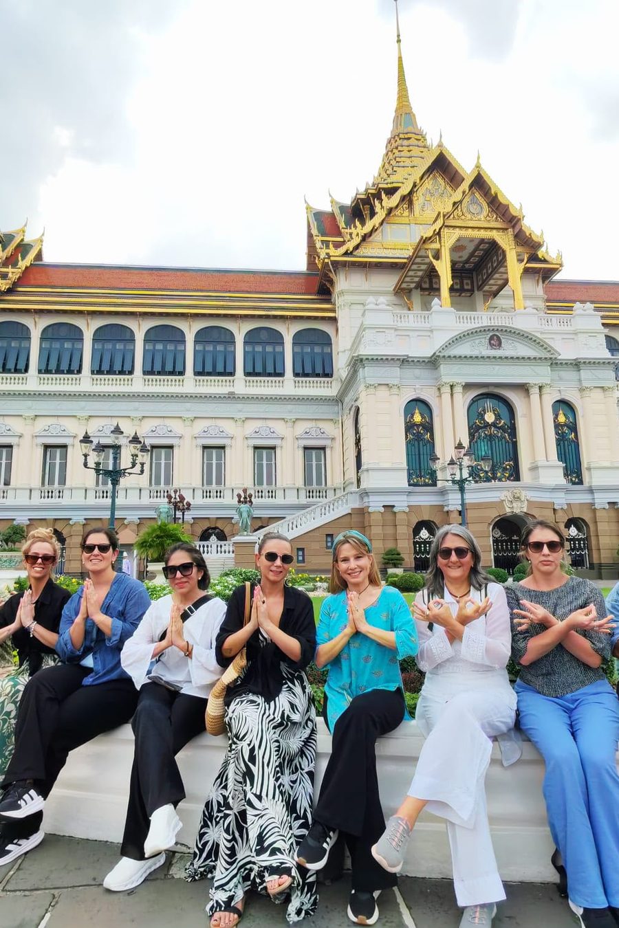 Grupo de viajeras haciendo el saludo con las manos frente al Gran Palacio de Bangkok